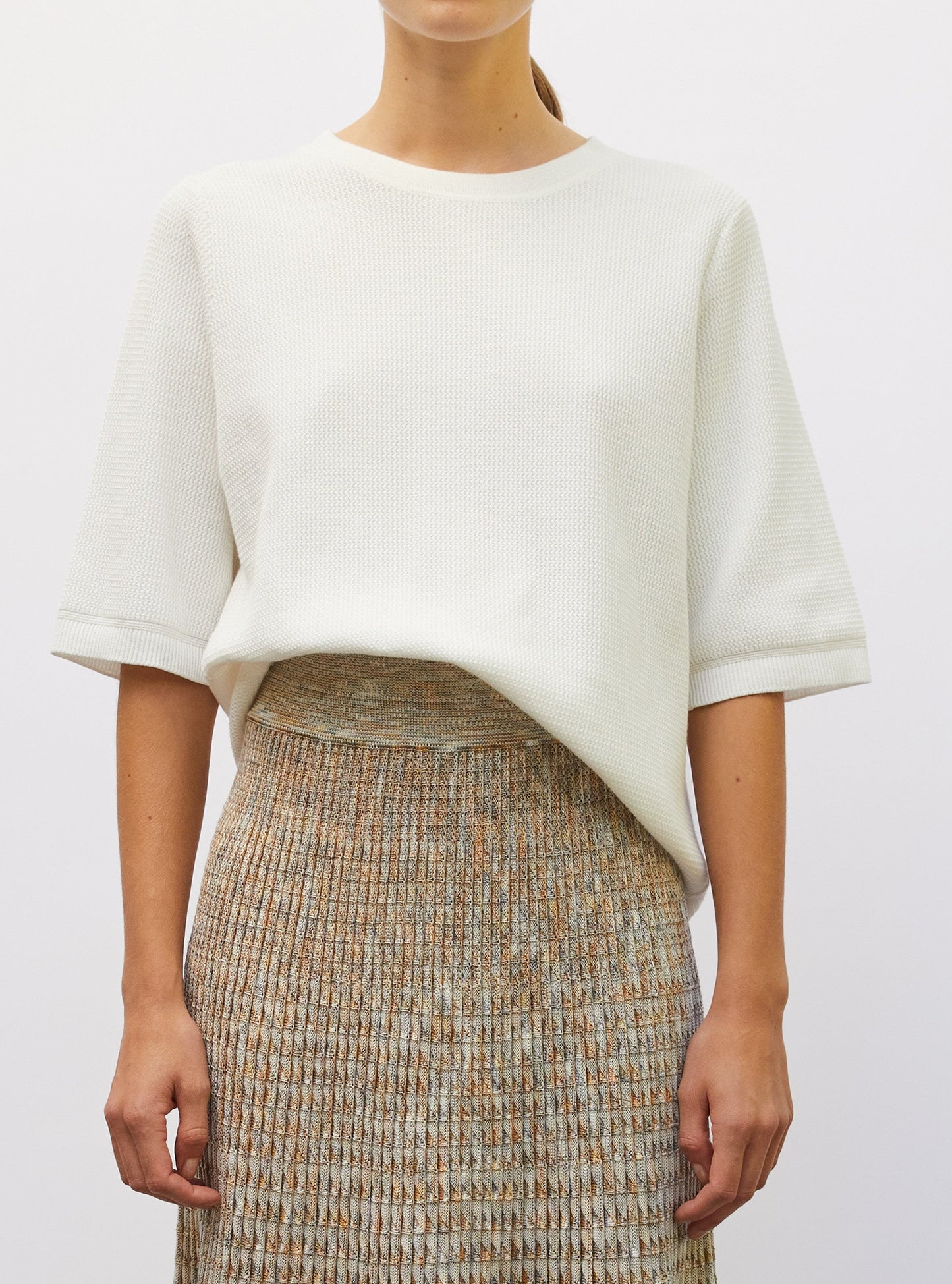 Woman wearing a white top and patterned skirt against a plain background