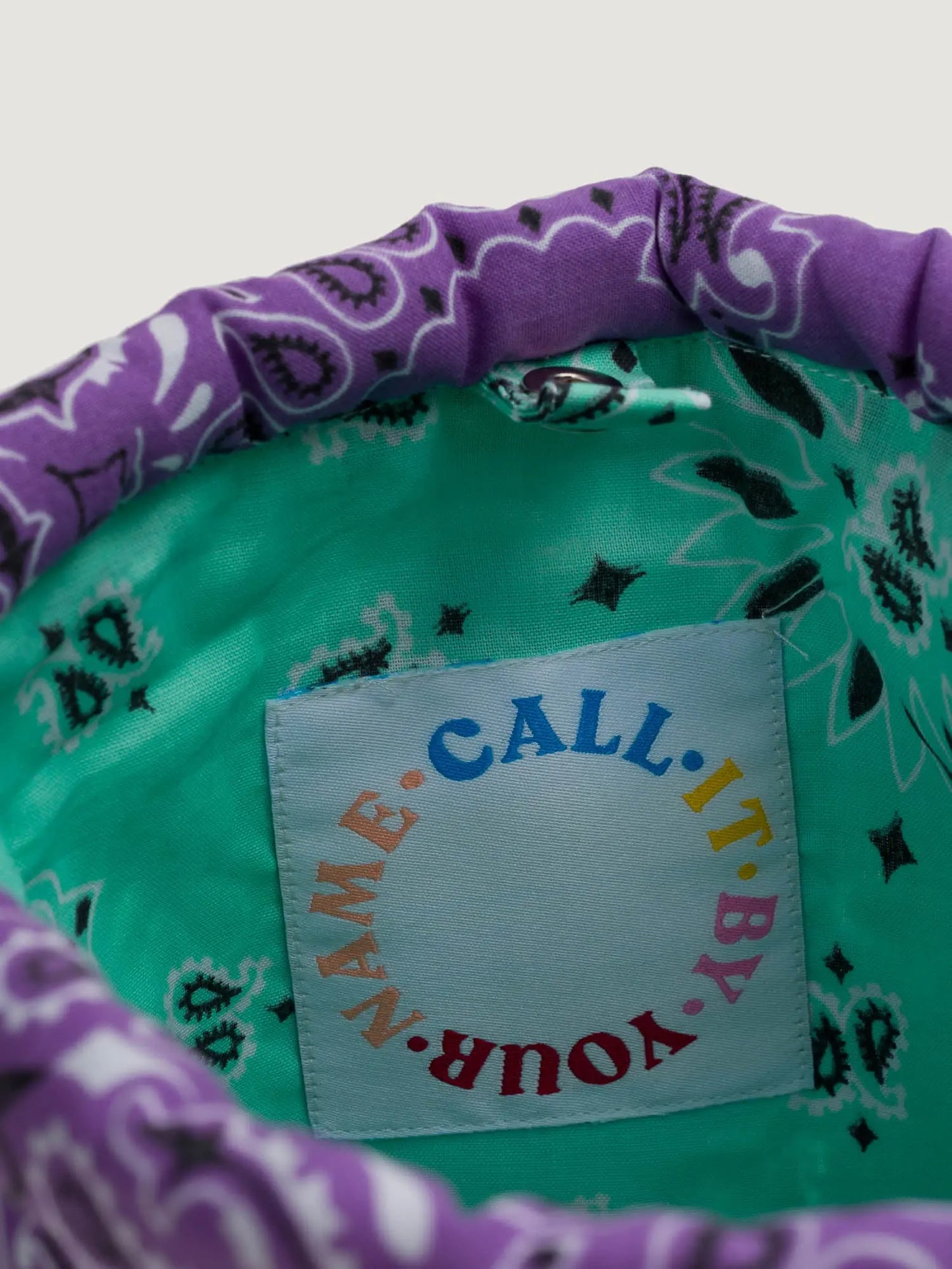 Purple and mint bandana bucket bag with adjustable strap, by brand Call it by your name, close-up on tag