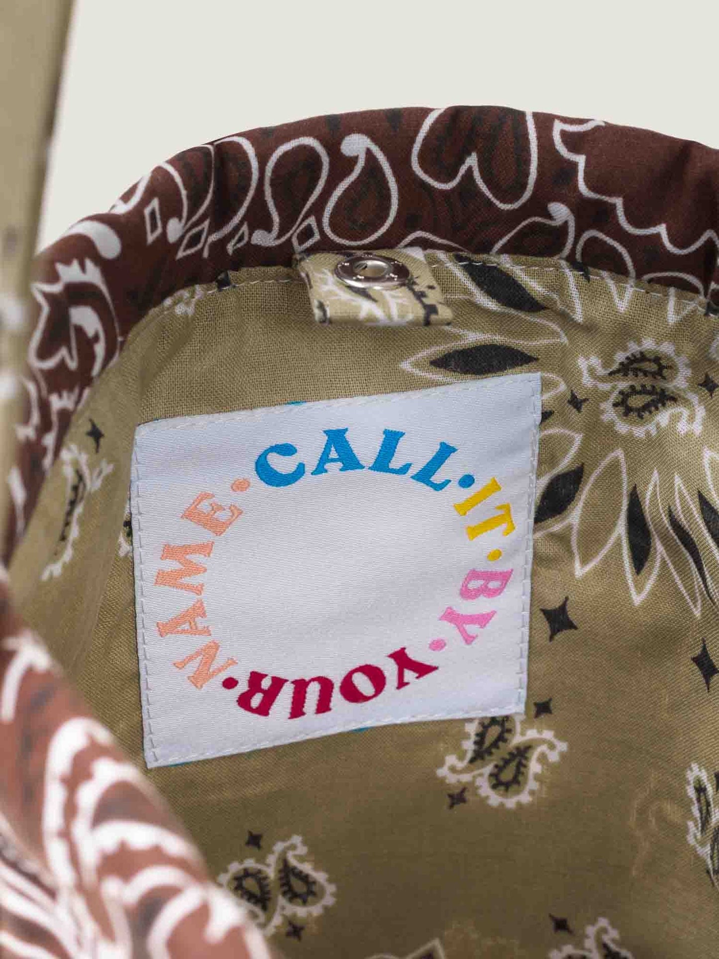 Brown and beige bandana bucket bag with adjustable strap, by brand Call it by your name, tag close-up