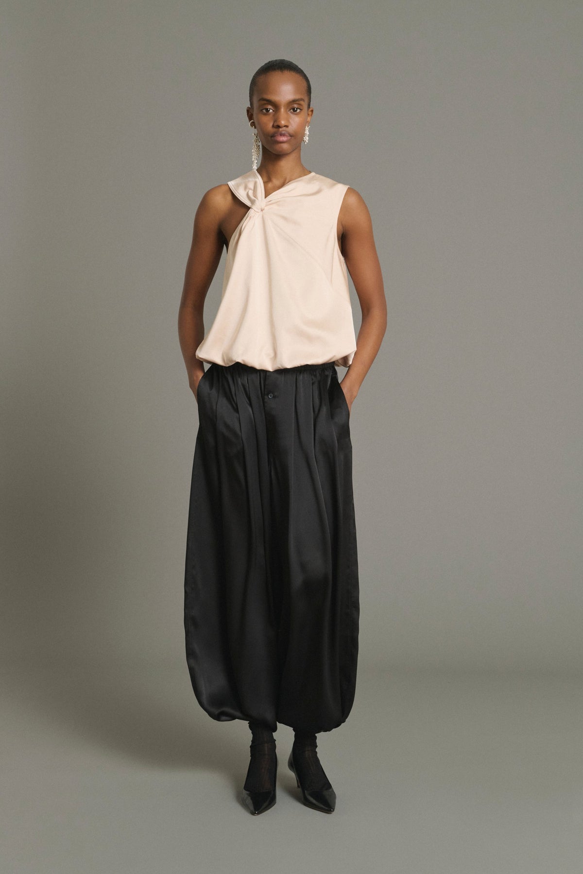 Model in the Soeur Leopold black silk satin balloon trousers with a beige halter top, front view