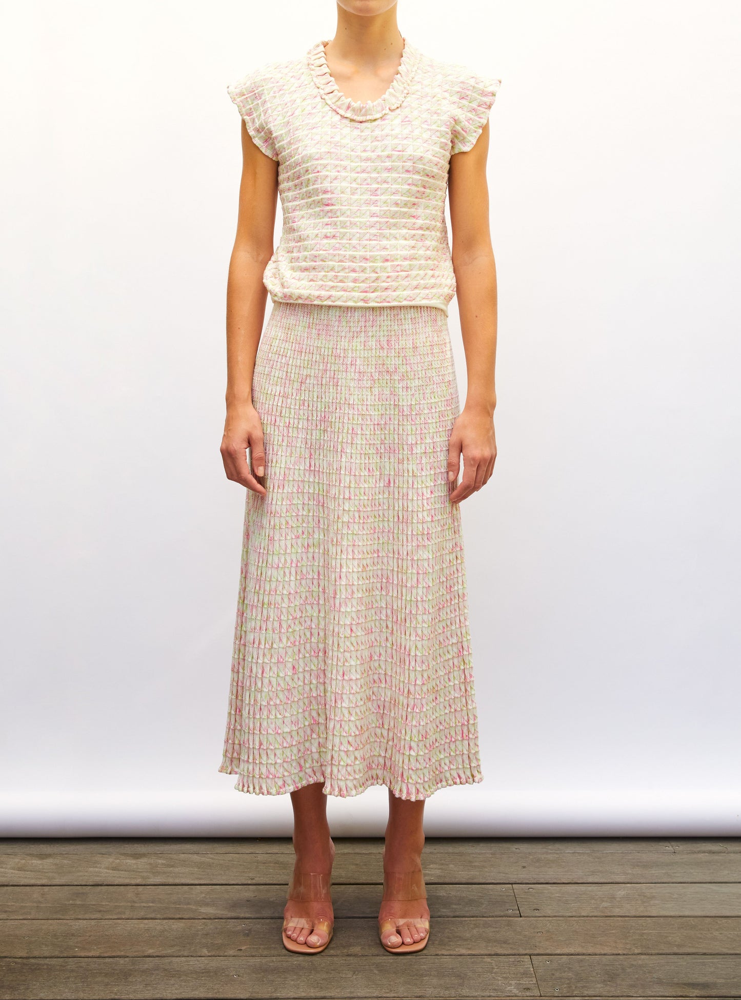 Woman wearing a light-colored origami knit top and origami knit skirt against a white background