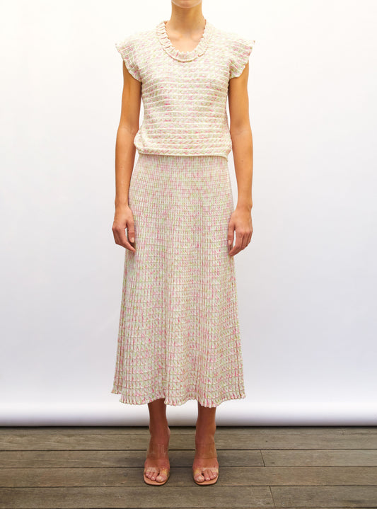 Woman wearing a light-colored origami knit top and origami knit skirt against a white background