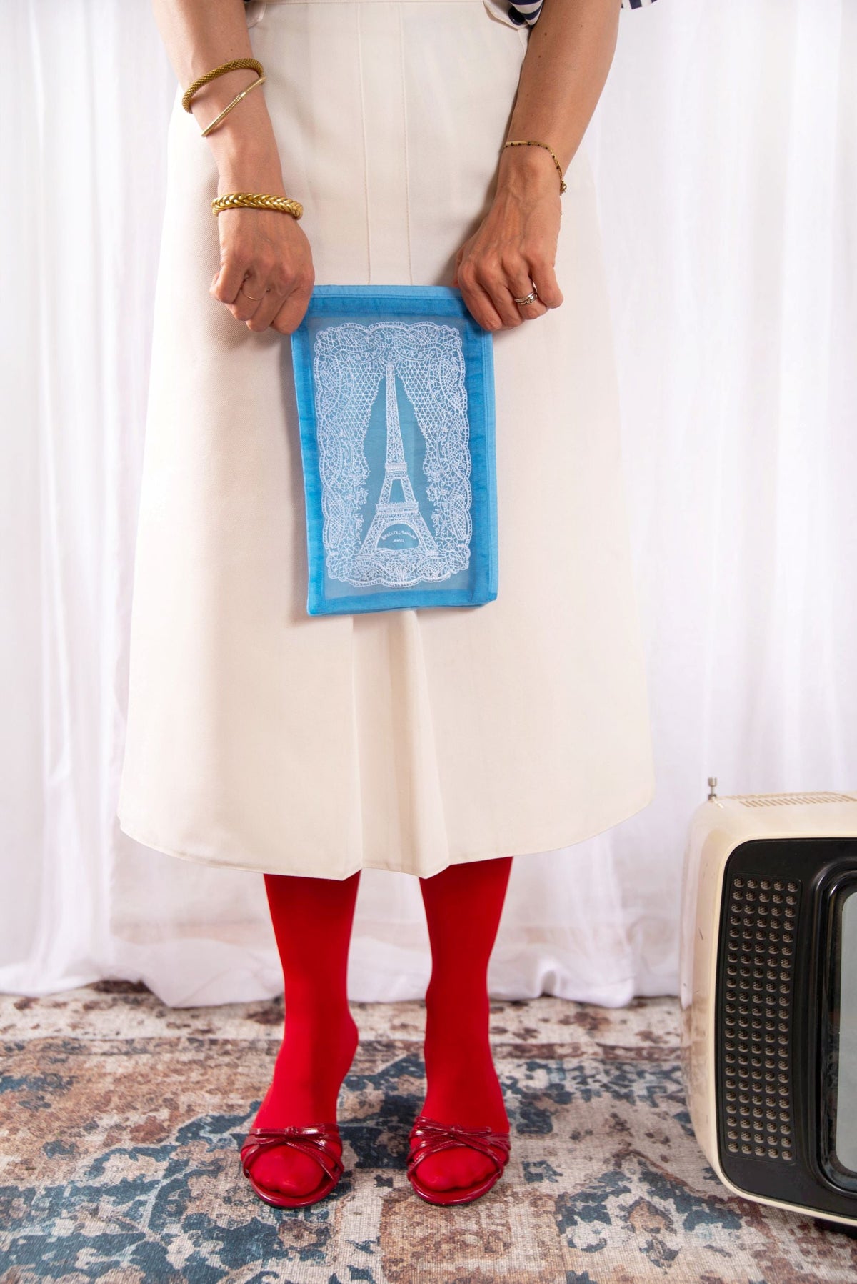 Model holding the Brigitte Tanaka blue Eiffel Tower lace pouch with a white dress and red socks