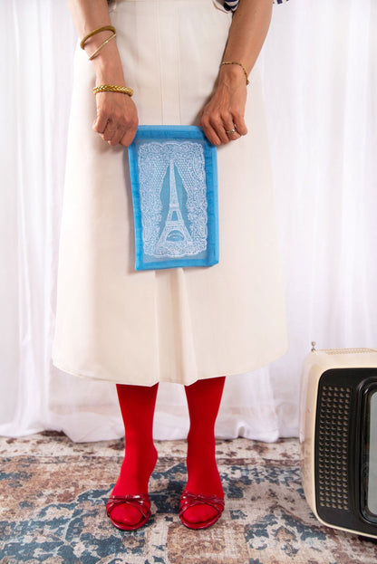 Model holding the Brigitte Tanaka blue Eiffel Tower lace pouch with a white dress and red socks