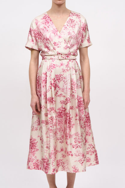 A woman modeling a short-sleeve midi wrap dress with a pink floral toile pattern on a cream background