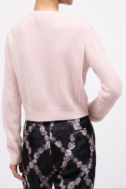 Woman wearing a light pink sweater and black pants with floral pattern on a white background