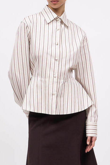 A model stands against a plain white studio background wearing a cream and brown vertically striped button-up shirt