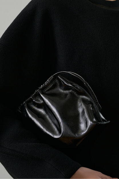 Person wearing a black sweater with a shiny black pouch on a gray background