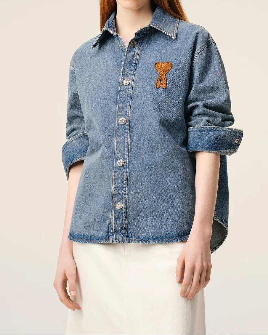 Woman wearing a blue denim shirt with a small embroidered design on a plain background
