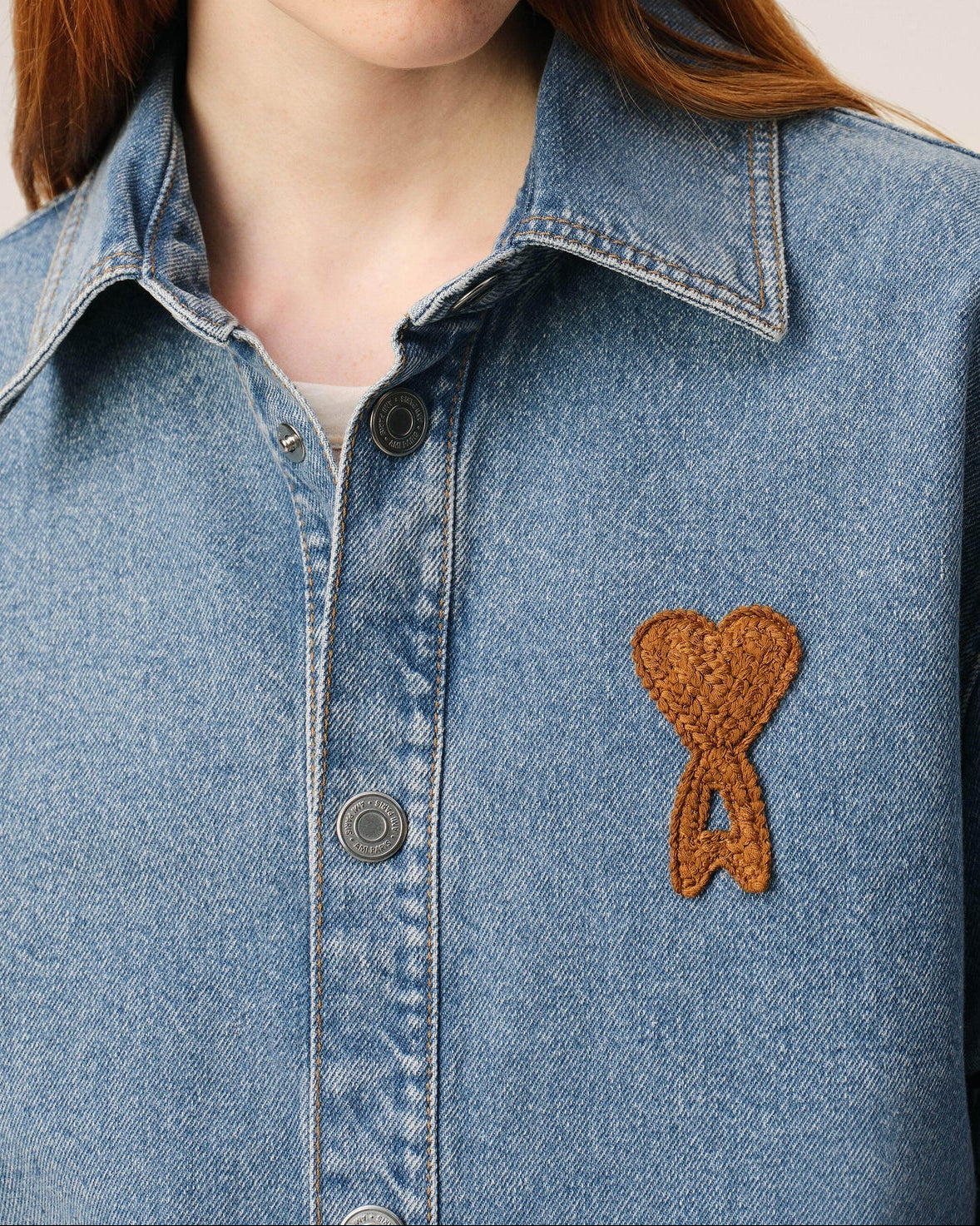 Blue denim shirt with a brown heart-shaped patch on a neutral background