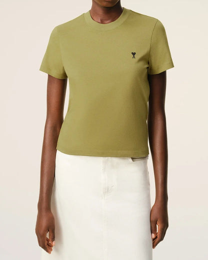 Person wearing a green t-shirt with a small logo on a beige background