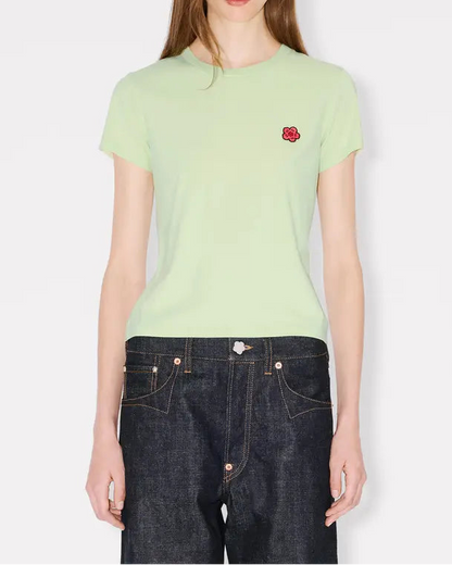 Person wearing a light green t-shirt with a red flower emblem on a white background
