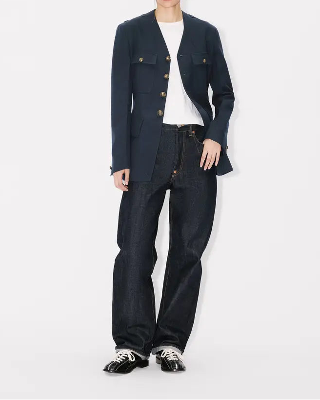 Person wearing a navy military blazer and dark jeans on a white background