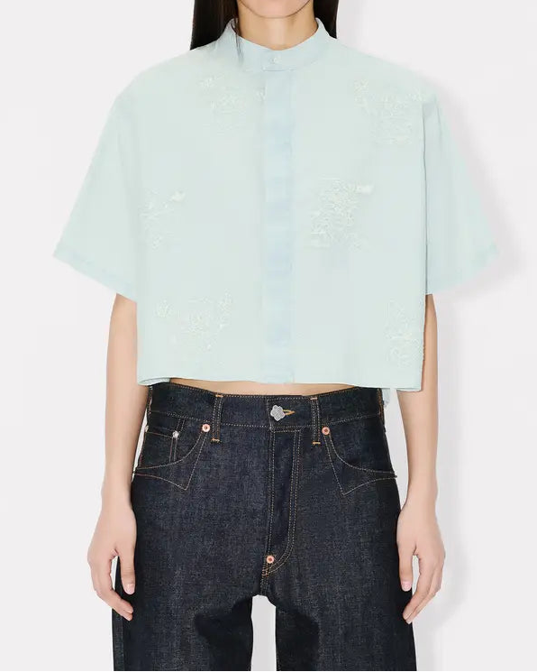Person wearing a light blue cropped top with cartoon embroidery and dark jeans on a white background