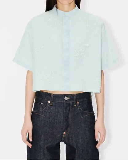 Person wearing a light blue cropped top with cartoon embroidery and dark jeans on a white background