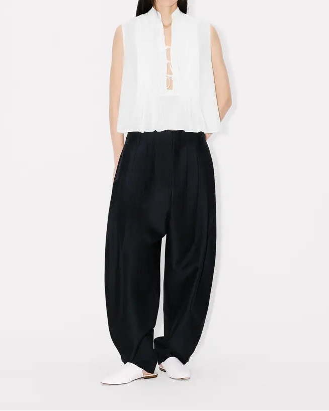 Person wearing a white sleeveless top and black pants on a white background