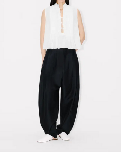 Person wearing a white sleeveless top and black pants on a white background