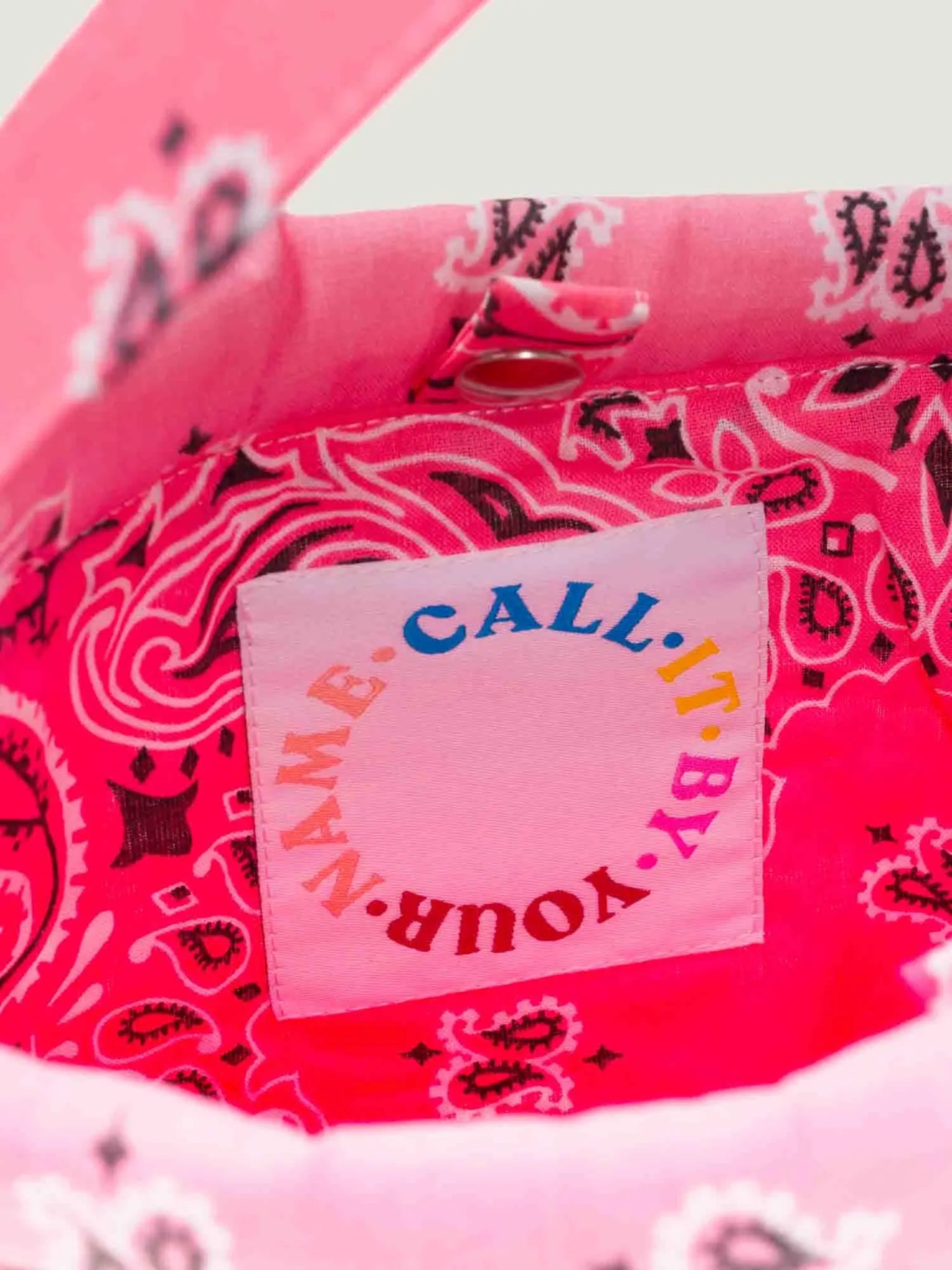 Pink bandana bucket bag with adjustable strap by brand call it by your name, close-up on tag