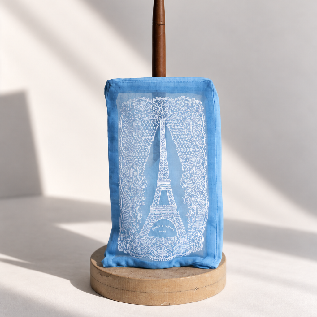 Brigitte Tanaka Eiffel Tower lace pouch in blue organza with white lace embroidery, on a wooden stand
