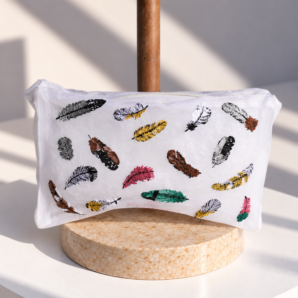 Brigitte Tanaka Feather pouch in white organza with multicolor feather embroidery, on a wooden stand