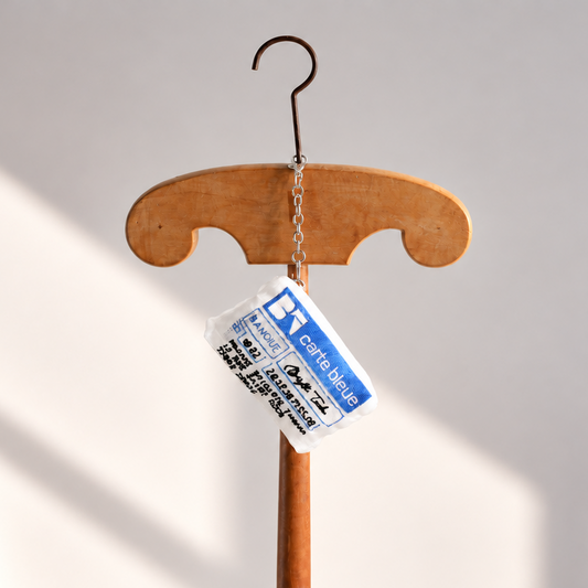 Brigitte Tanaka bank card mini pouch in white organza with blue embroidery, hanging from a wooden hanger